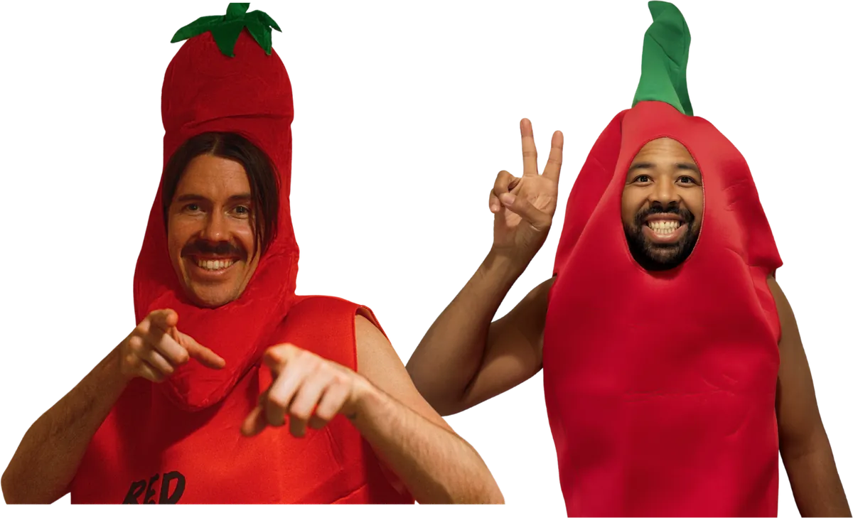 Mitchell and Takashi of Spice Agency smiling in red chili pepper costumes, one pointing at the camera and one giving a peace sign